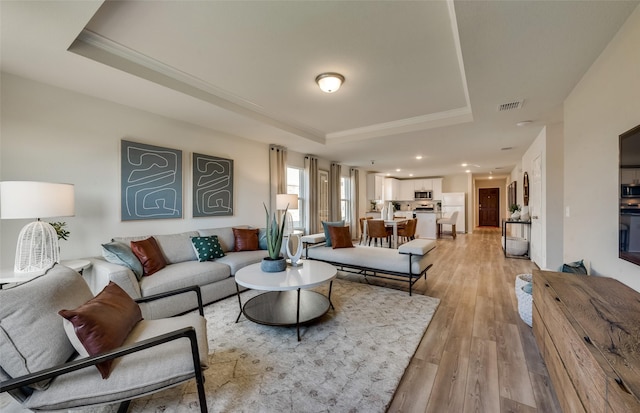 living area featuring visible vents, crown molding, light wood-type flooring, and a tray ceiling