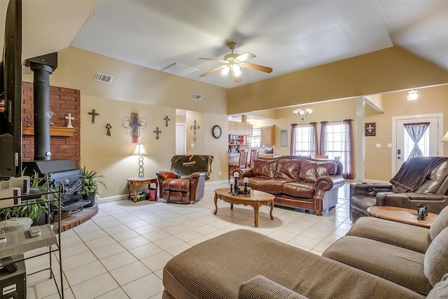 living room featuring visible vents, ceiling fan with notable chandelier, light tile patterned floors, a wood stove, and vaulted ceiling