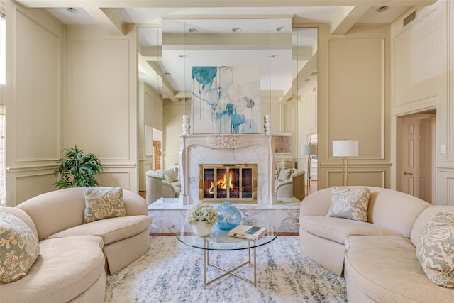 living room with visible vents, beamed ceiling, a premium fireplace, and a decorative wall