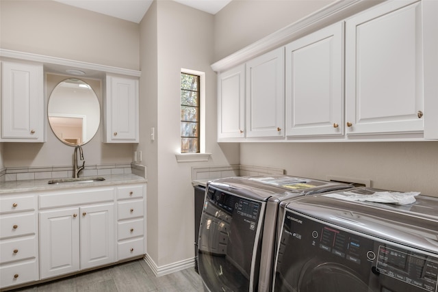 clothes washing area with baseboards, cabinet space, a sink, light wood-style floors, and washer and dryer