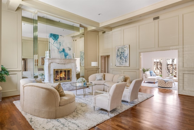 living area featuring wood finished floors, visible vents, a premium fireplace, beam ceiling, and a decorative wall