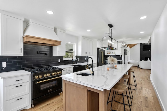 kitchen with premium range hood, a center island with sink, high end refrigerator, gas stove, and a sink