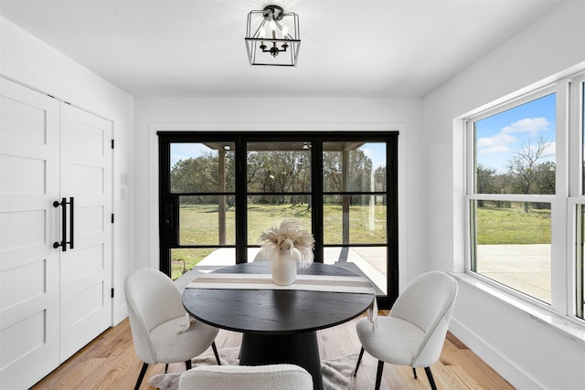 dining room featuring a healthy amount of sunlight, an inviting chandelier, light wood-style flooring, and baseboards