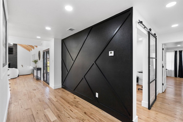 hall with light wood finished floors, visible vents, recessed lighting, and a barn door