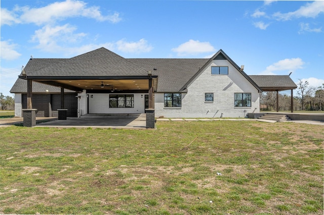 rear view of property with ceiling fan, a yard, a shingled roof, and a patio area