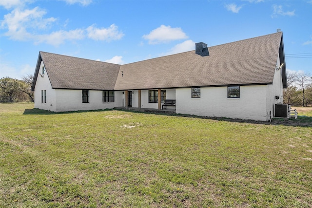 back of house with a chimney, central AC unit, a lawn, and a shingled roof