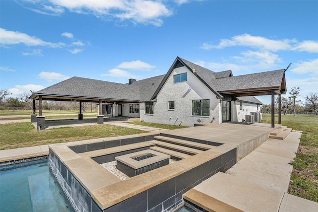 rear view of house featuring a patio, a fire pit, a lawn, and roof with shingles