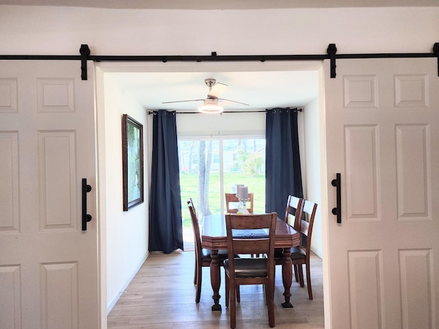 dining room featuring a barn door, light wood-style flooring, and a ceiling fan