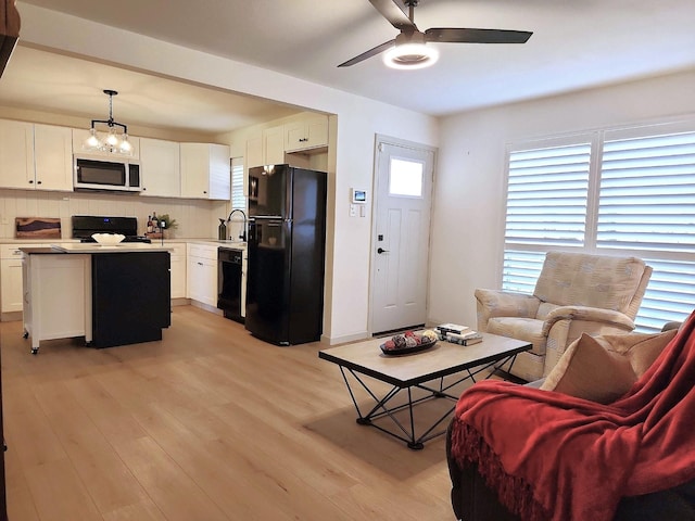 living area featuring plenty of natural light, ceiling fan with notable chandelier, and light wood-type flooring