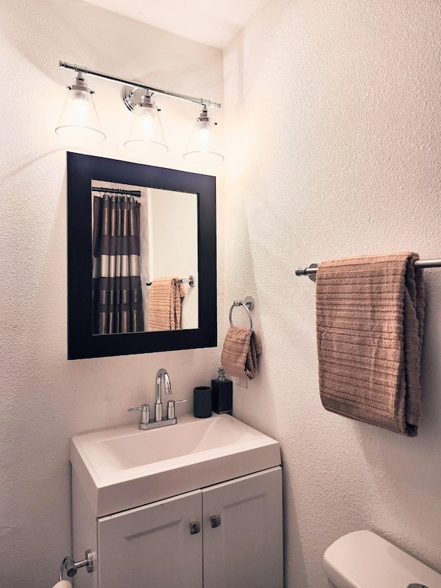 bathroom featuring vanity, toilet, and a textured wall