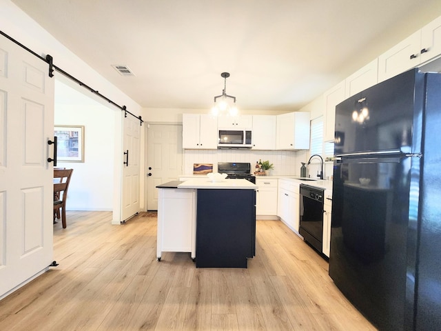 kitchen featuring light wood-style flooring, a sink, black appliances, white cabinets, and a barn door