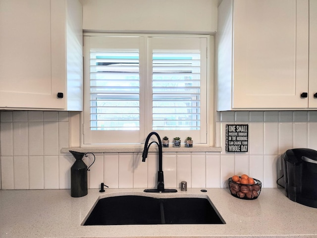 kitchen with white cabinetry, light stone counters, backsplash, and a sink