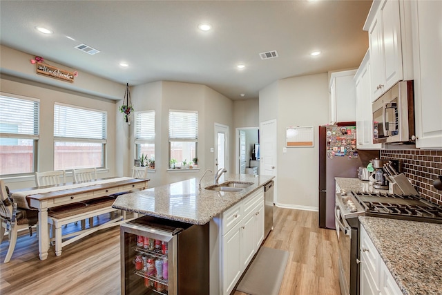 kitchen featuring visible vents, beverage cooler, a sink, stainless steel appliances, and light wood finished floors