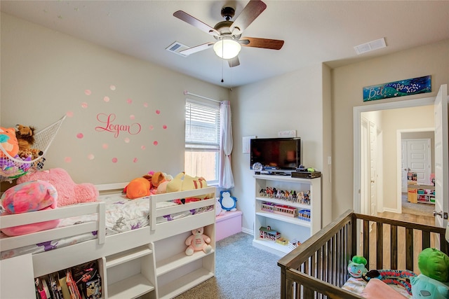 carpeted bedroom featuring baseboards, visible vents, a crib, and a ceiling fan