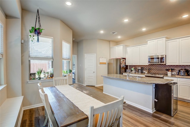 kitchen with visible vents, backsplash, a center island with sink, light wood-type flooring, and stainless steel appliances