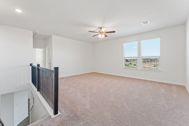 carpeted spare room with visible vents, baseboards, attic access, and ceiling fan