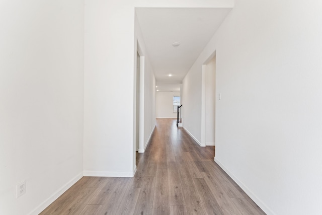 hall featuring an upstairs landing, light wood-style flooring, and baseboards