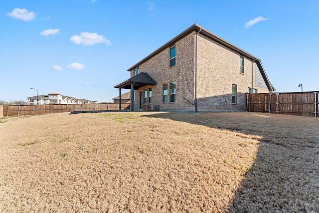 back of property with a yard, brick siding, and fence