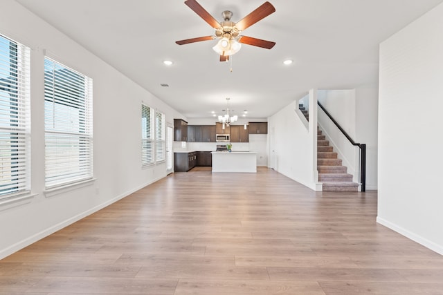 unfurnished living room featuring recessed lighting, stairway, light wood-style floors, and ceiling fan with notable chandelier