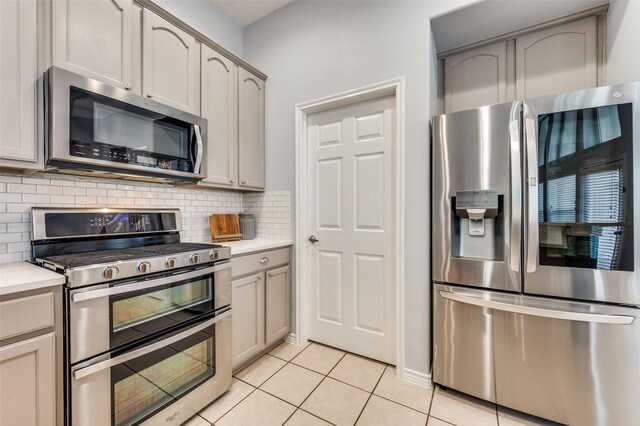 kitchen with tasteful backsplash, gray cabinetry, light countertops, light tile patterned flooring, and stainless steel appliances