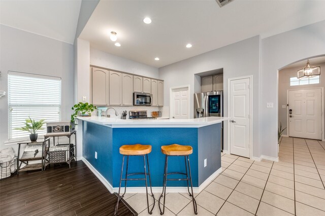 kitchen with a peninsula, arched walkways, stainless steel appliances, light countertops, and tasteful backsplash