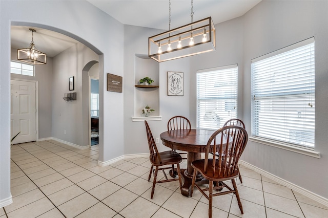 dining room featuring light tile patterned flooring, baseboards, arched walkways, and plenty of natural light