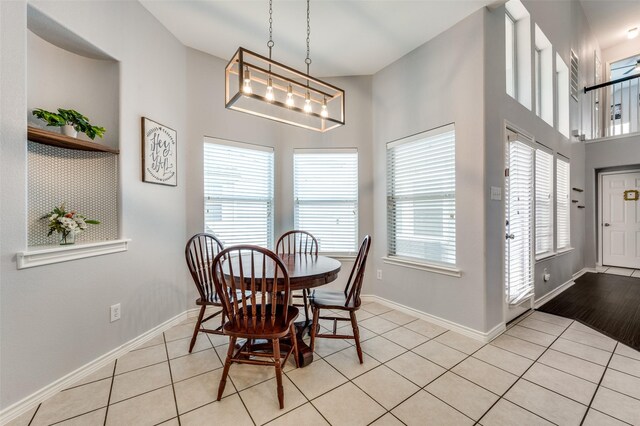 dining area featuring light tile patterned floors, baseboards, a notable chandelier, and a towering ceiling