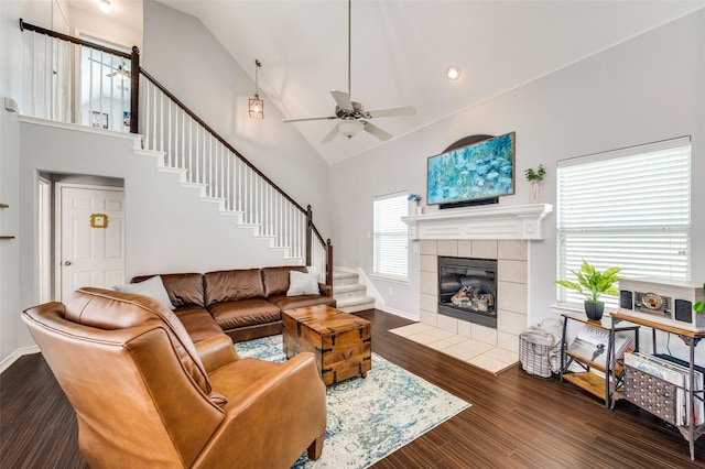 living room featuring a tiled fireplace, stairway, dark wood-style floors, high vaulted ceiling, and a ceiling fan