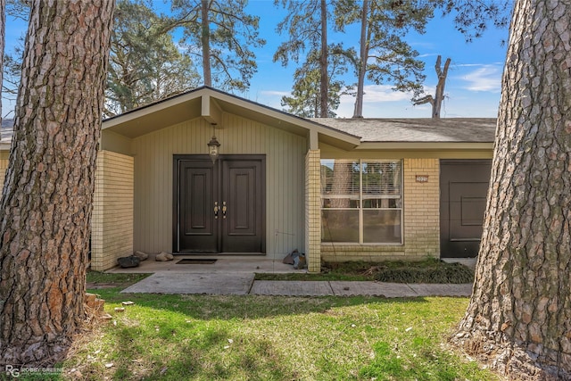 doorway to property with a lawn and brick siding