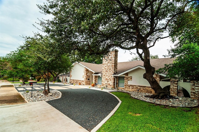 view of front of house with roof with shingles, stucco siding, a chimney, stone siding, and driveway