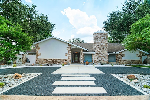 view of front of property with stone siding, a chimney, and a shingled roof