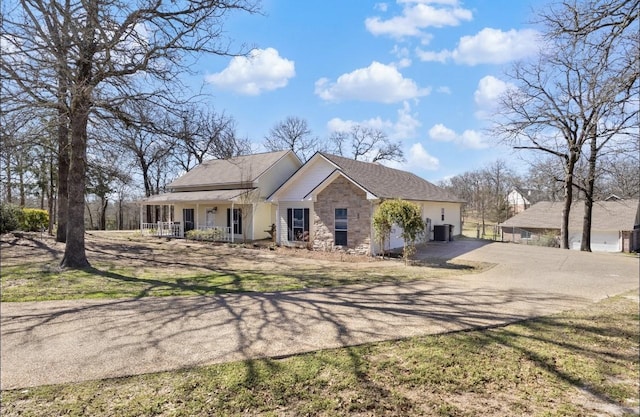 view of front facade with a porch, cooling unit, stone siding, and dirt driveway