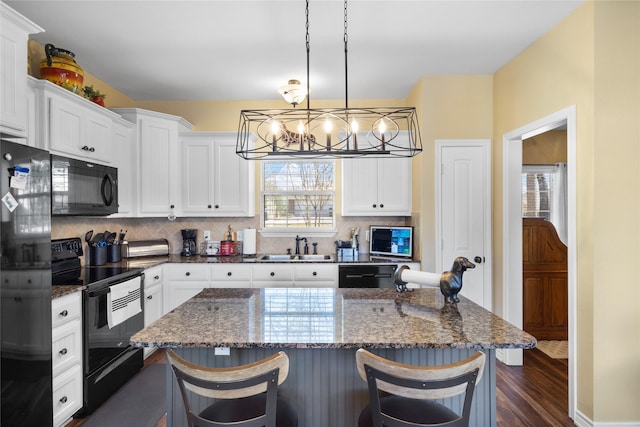 kitchen with decorative backsplash, black appliances, a kitchen breakfast bar, and a sink