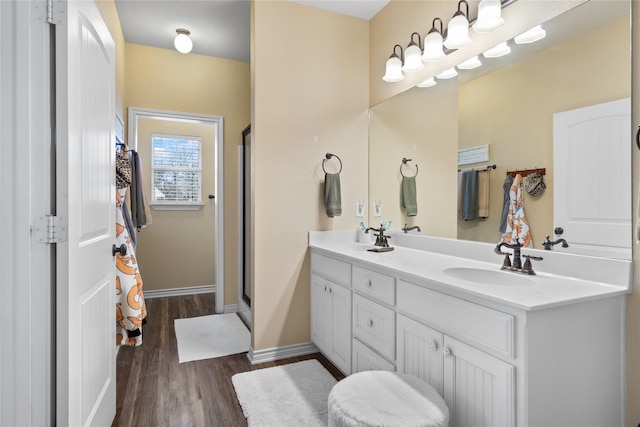 full bathroom with double vanity, wood finished floors, a stall shower, and a sink