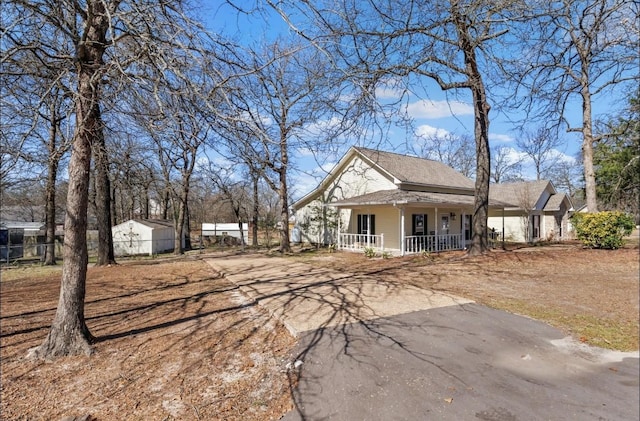 view of front of house featuring aphalt driveway, covered porch, and fence