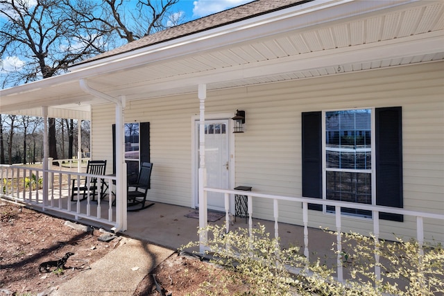 entrance to property featuring a porch and a shingled roof