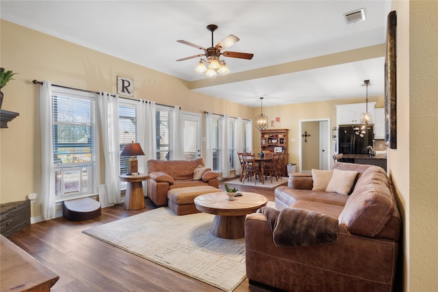 living area with baseboards, wood finished floors, visible vents, and ceiling fan