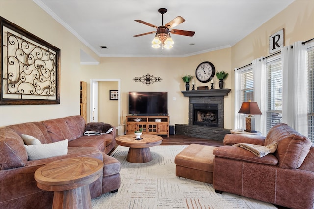 living room featuring visible vents, crown molding, ceiling fan, a fireplace, and wood finished floors