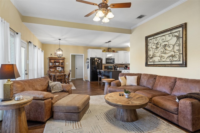 living area with visible vents, baseboards, dark wood-type flooring, crown molding, and ceiling fan with notable chandelier