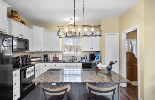 kitchen with tasteful backsplash, a breakfast bar area, black appliances, and a sink