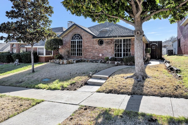 single story home with brick siding, cooling unit, a shingled roof, and a chimney