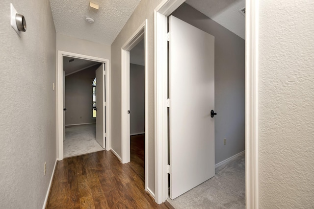 hallway with wood finished floors, baseboards, a textured wall, and a textured ceiling