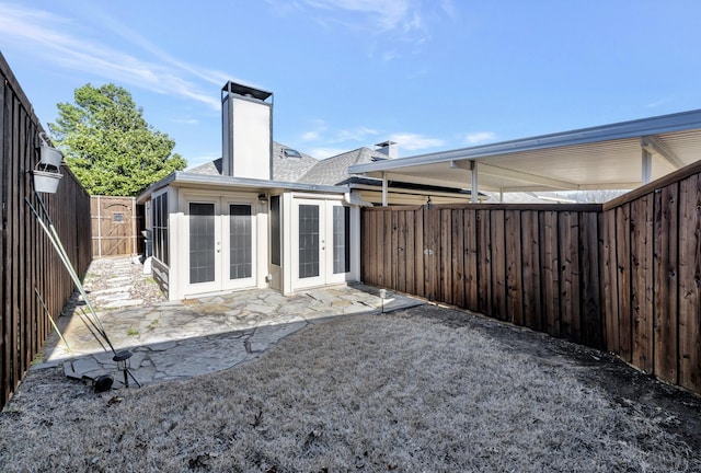 rear view of house with roof with shingles, a fenced backyard, a chimney, french doors, and a patio area