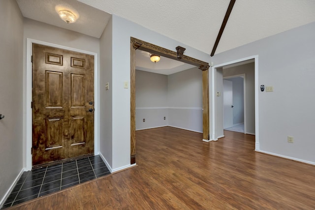 foyer with baseboards, a textured ceiling, dark wood-style floors, and vaulted ceiling