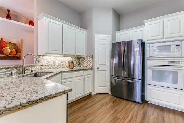 kitchen with a sink, light stone counters, white appliances, light wood-style floors, and decorative backsplash