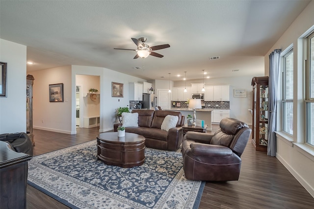 living room with baseboards, a ceiling fan, and dark wood-style flooring