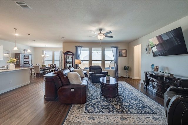 living room featuring visible vents, baseboards, dark wood-type flooring, and ceiling fan with notable chandelier