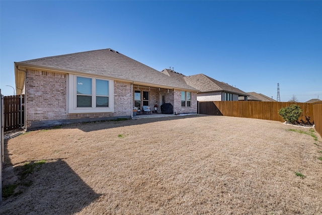 rear view of house with a patio, a fenced backyard, brick siding, and roof with shingles