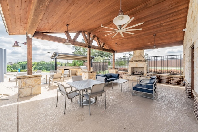 view of patio / terrace with outdoor dining space, a ceiling fan, an outdoor living space with a fireplace, fence, and exterior kitchen