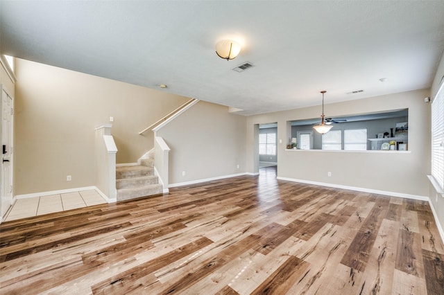 unfurnished living room with stairway, baseboards, visible vents, and light wood-type flooring